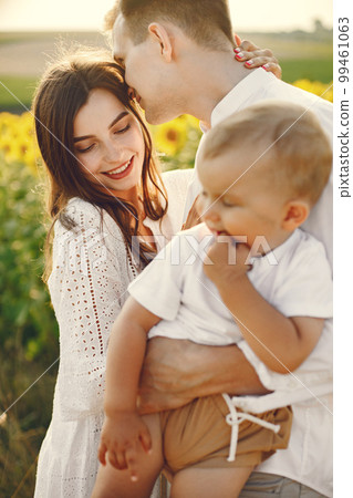 Photo of a young family at the sunflowers field on a sunny day. Brunette mother, father and their little blonde son posing for a photo. Man and woman hugging their son. Photo of a young family at the sunflowers field on a sunny day. Brunette mother, father and their little blonde son posing for a photo. Man and woman hugging their son. 99461063