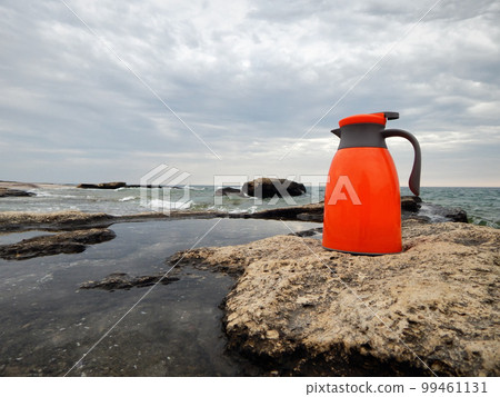 Orange thermos on the shore. Orange thermos on the shore. 99461131