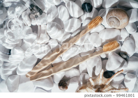 Two eco bamboo toothbrushes with natural bristles in transparent fresh water with waves on bottom of stones and shells 99461801