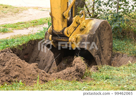 A bucket of a bulldozer digs the ground with a grass close-up in an industrial area. Excavation work on the construction site 99462065