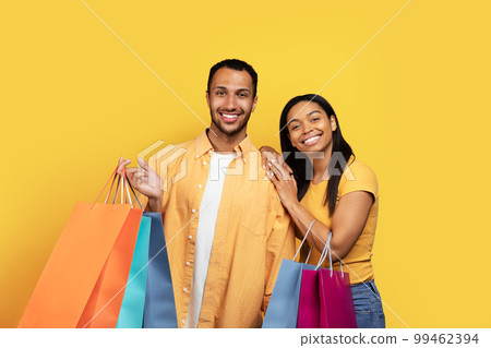 Glad young african american male and woman shopaholics hold many packages with purchases Glad young african american male and woman shopaholics hold many packages with purchases 99462394