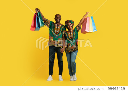 Happy african american couple in national costumes holding shopping bags Happy african american couple in national costumes holding shopping bags 99462419