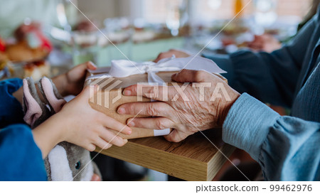 Close-up of grandmother giving gift to her granddaughter during Easter dinner. Close-up of grandmother giving gift to her granddaughter during Easter dinner. 99462976