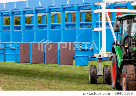 Blue horse racing starting gate on start by tractor machine at equiestrian racehorse hippodrome. Outdoor sport racecourse competition equipment Blue horse racing starting gate on start by tractor machine at equiestrian racehorse hippodrome. Outdoor sport racecourse competition equipment 99463199