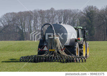 Green tractor with a manure truck on a grass field Green tractor with a manure truck on a grass field 99463375