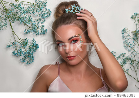 Portrait of a smiling beautiful, sweet girl on a white background with white and blue flowers. 99463395