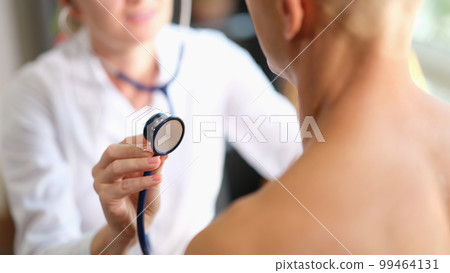 The doctor is touched by a stethoscope in a man, close-up The doctor is touched by a stethoscope in a man, close-up 99464131
