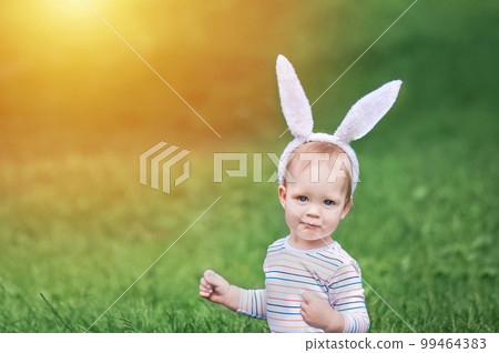 Toddler boy egg hunter close-up in grass with bunny ears... 99464383