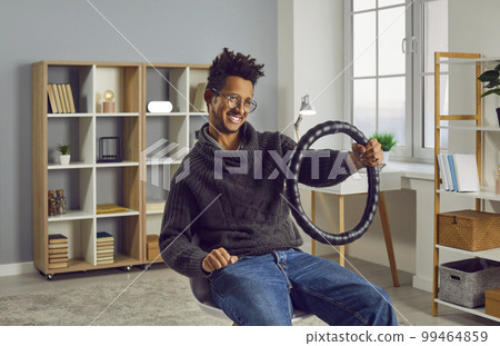 Funny, happy young African American man pretending to drive an invisible car indoors 99464859