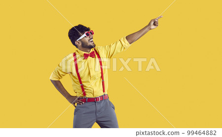 Young funny Indian man with smile points to copy space for promotional offer on yellow background 99464882
