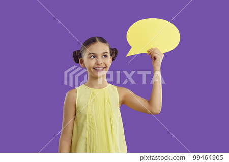 Happy cheerful child isolated on purple background holding yellow speech balloon Happy cheerful child isolated on purple background holding yellow speech balloon 99464905