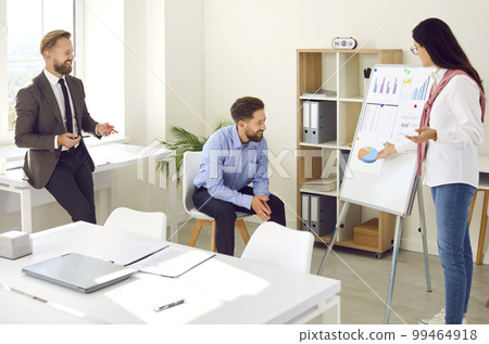 Young woman giving a presentation by an office white board during a business team meeting Young woman giving a presentation by an office white board during a business team meeting 99464918