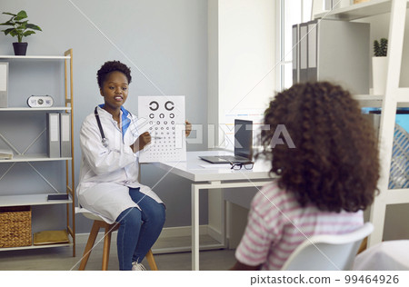 Female optometrist examines vision of child girl patient using vision chart in hospital office. 99464926