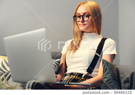Young woman working on laptop at home, sitting on the sofa. Concept during coronavirus Young woman working on laptop at home, sitting on the sofa. Concept during coronavirus 99466528