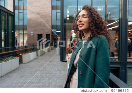 Portrait of young woman in green coat with curly hair in the city 99466855