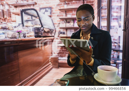 Young african woman sitting in arm-chair and using digital tablet 99466856