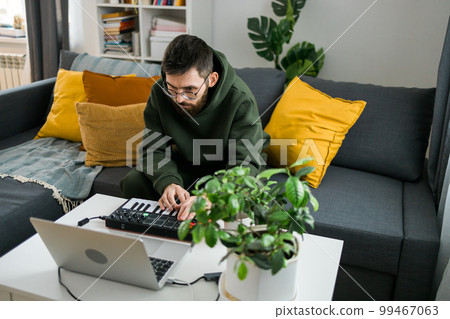 Man recording electronic music track with portable midi keyboard on laptop computer in home studio. Producing and mixing music beat making and arranging audio content with professional audio devices 99467063
