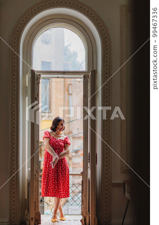 a beautiful and happy brunette women in red retro dress in the balcony doorway  99467336