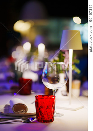 a table with a white tablecloth, glasses, crockery and decor in dark restaurant 99467355