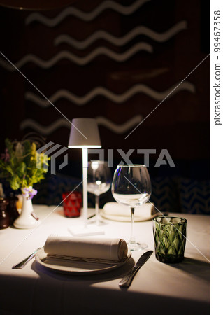 a table with a white tablecloth, glasses, crockery and decor in dark restaurant a table with a white tablecloth, glasses, crockery and decor in dark restaurant 99467358