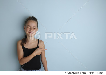 Little emotional teenage girl in a black t-shirt 11, 12 years old on an isolated blue background. Children's studio portrait. Place the text to copy the place for the inscription 99467484