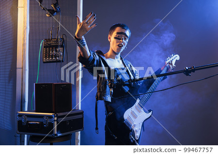 Woman artist with crazy make up creating cool vibe, doing live performance with rock and heavy metal music. Stylish solo musician with guitar doing concert and screaming loud, studio with smoke. Woman artist with crazy make up creating cool vibe, doing live performance with rock and heavy metal music. Stylish solo musician with guitar doing concert and screaming loud, studio with smoke. 99467757