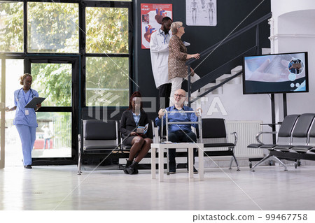 Elderly man patient with walking frame sitting in hospital waiting area discussing medical insurance with receptionist during checkup visit consultation. Medicine service and concept Elderly man patient with walking frame sitting in hospital waiting area discussing medical insurance with receptionist during checkup visit consultation. Medicine service and concept 99467758