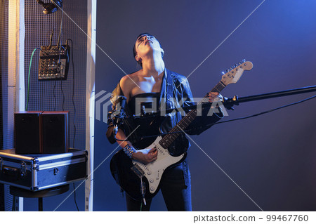 Woman rocker playing alternative guitar and performing heavy metal concert, using microphone to sing cool song and instrument. Artist feeling ecstatic about live rock performance, crazy make up. Woman rocker playing alternative guitar and performing heavy metal concert, using microphone to sing cool song and instrument. Artist feeling ecstatic about live rock performance, crazy make up. 99467760