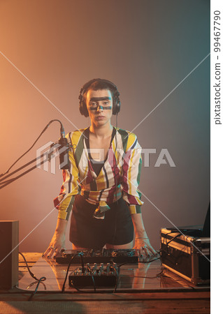 Female DJ standing at turntables and mixing equipment, using audio instruments or mixer to perform techno music. Serious musician with crazy make up doing remix with bass key and buttons. 99467790