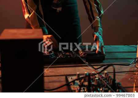 Musical artist mixing techno music on turntables, playing record mix sounds on audio dj instrument and stereo equipment. Enjoying nightclub party with stage production on studio background. 99467803