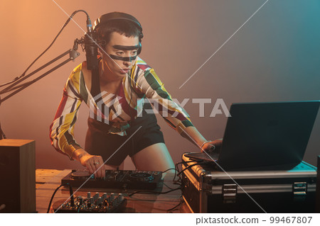 Musical performer using turntables to mix techno music, producing sounds at dj mixer with electronics and bass key. Woman working as artist doing remix performance at nightclub in studio. 99467807