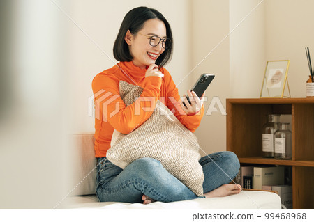 A woman looking at her smartphone on the sofa at home 99468968