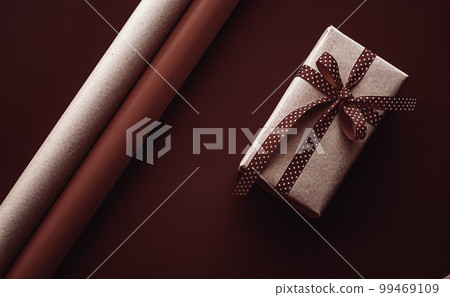Gifts preparation, birthday and holidays gift giving, craft paper and ribbons for gift boxes on chocolate background as wrapping tools and decorations, diy presents as holiday flat lay design. 99469109