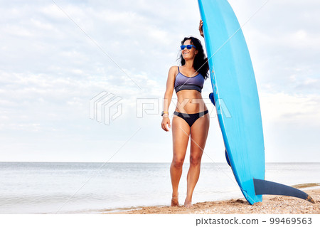 Young woman with surf stands on the beach 99469563