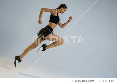 Determined sporty woman running in Mid-Air exercising during cardio workout over studio background 99470349