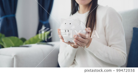 Young asian woman holding white piggy bank at home. Save money and investment concept 99472038
