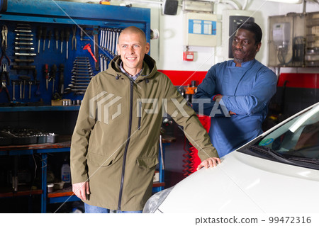 Portrait of satisfied male client with mechanician standing near her car after repairing in workshop 99472316