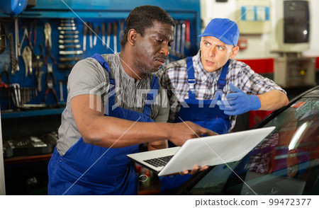 Two auto mechanics diagnosing car engine with laptop Two auto mechanics diagnosing car engine with laptop 99472377