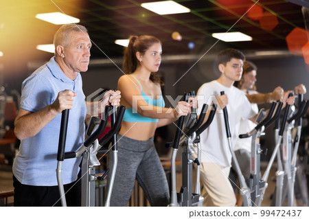 Aged man doing cardio workout on elliptical machine in gym Aged man doing cardio workout on elliptical machine in gym 99472437