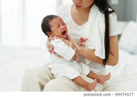 mother holding burping and crying baby in bedroom after feeding milk 99474577