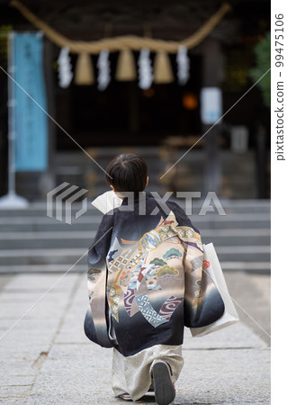 穿著日式服裝前來參拜 Shichi-go-san 神社的 5 歲男孩的身影在神社範圍內單手拿著折扇擺姿勢（特寫，後視圖） 99475106
