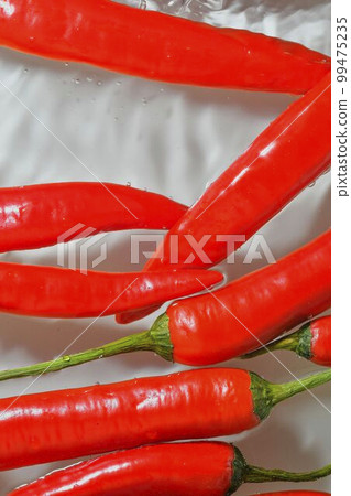 Red hot peppers in water splash on white background. Splashing water and bubbles. Vertical image, close-up Red hot peppers in water splash on white background. Splashing water and bubbles. Vertical image, close-up 99475235