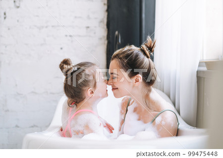 Young mother woman and little tween girl daughter having fun in bath with foam at home Young mother woman and little tween girl daughter having fun in bath with foam at home 99475448