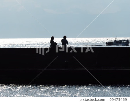 Silhouette of two people sitting on the beach 99475469