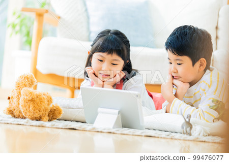 Siblings watching videos in the living room Siblings watching videos in the living room 99476077