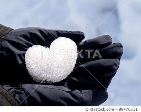 A heart made of snow is placed on the gloved hand. 99476511