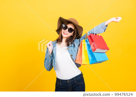Asian happy portrait beautiful cute young woman teen smiling standing with sunglasses excited holding shopping bags multi color looking camera isolated, studio shot yellow background with copy space Asian happy portrait beautiful cute young woman teen smiling standing with sunglasses excited holding shopping bags multi color looking camera isolated, studio shot yellow background with copy space 99476524