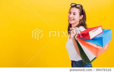 Asian Thai portrait happy beautiful cute young woman smiling stand with sunglasses excited holding shopping bags multi color looking side, studio shot isolated yellow background with copy space Asian Thai portrait happy beautiful cute young woman smiling stand with sunglasses excited holding shopping bags multi color looking side, studio shot isolated yellow background with copy space 99476526