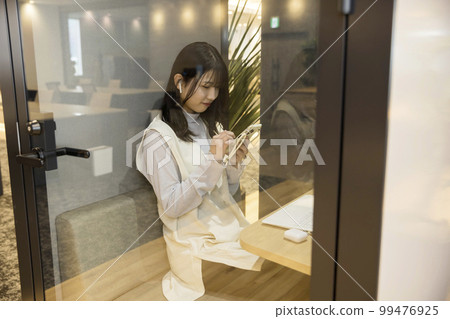 A young woman operating a smartphone in a private room booth in a design office A young woman operating a smartphone in a private room booth in a design office 99476925