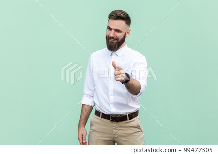 Hey, I choose you. Portrait of attractive flirting bearded businessman wearing white shirt pointing finger and winking at camera, choosing you. Indoor studio shot isolated on light green background. Hey, I choose you. Portrait of attractive flirting bearded businessman wearing white shirt pointing finger and winking at camera, choosing you. Indoor studio shot isolated on light green background. 99477305